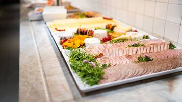 A buffet table with various food items including sliced meats, cheeses, and fruits.