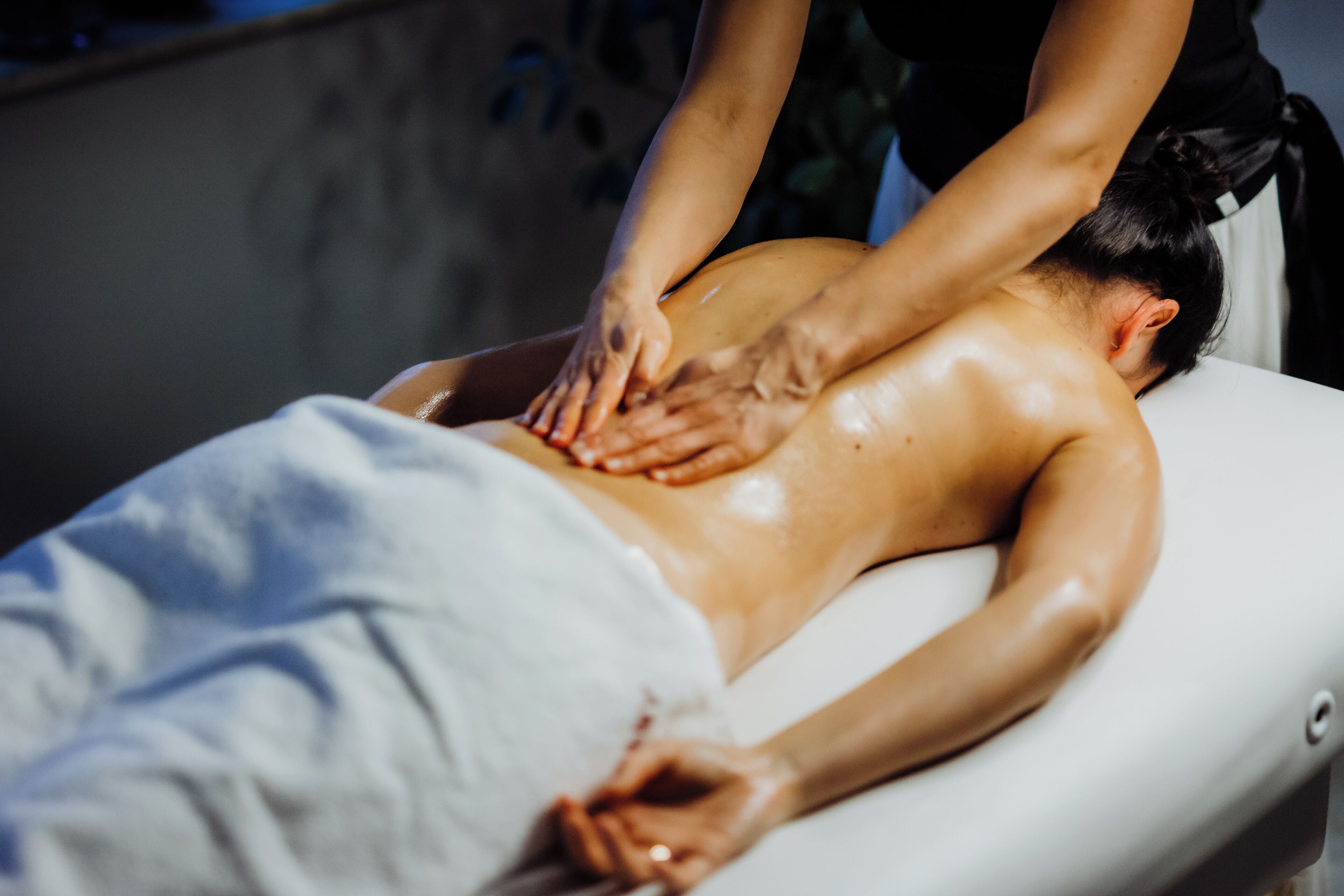 A person receiving a back massage on a massage table in a room with a plain wall and a window.