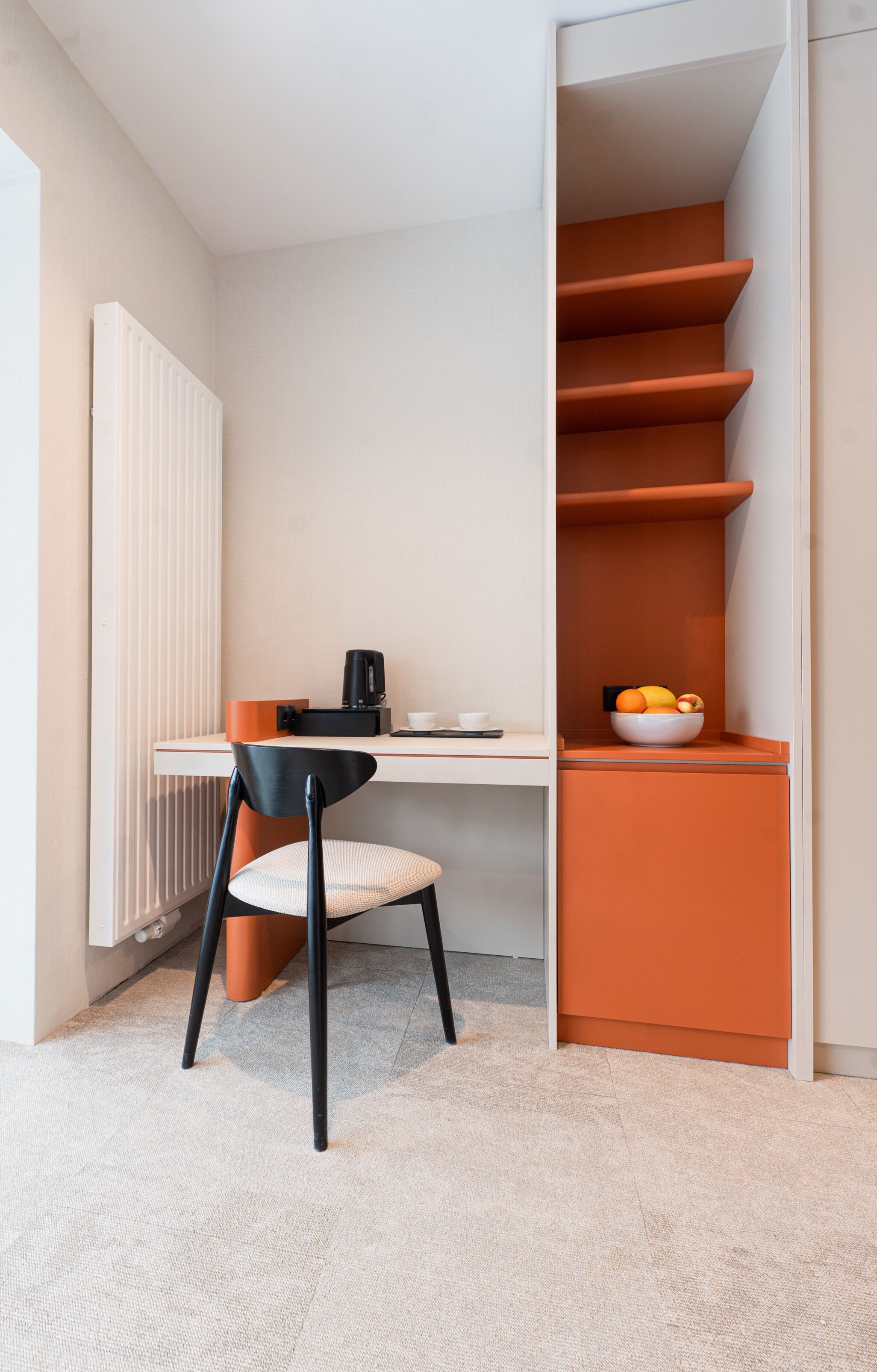 A modern room with a desk, chair, and a fruit bowl on a shelf.