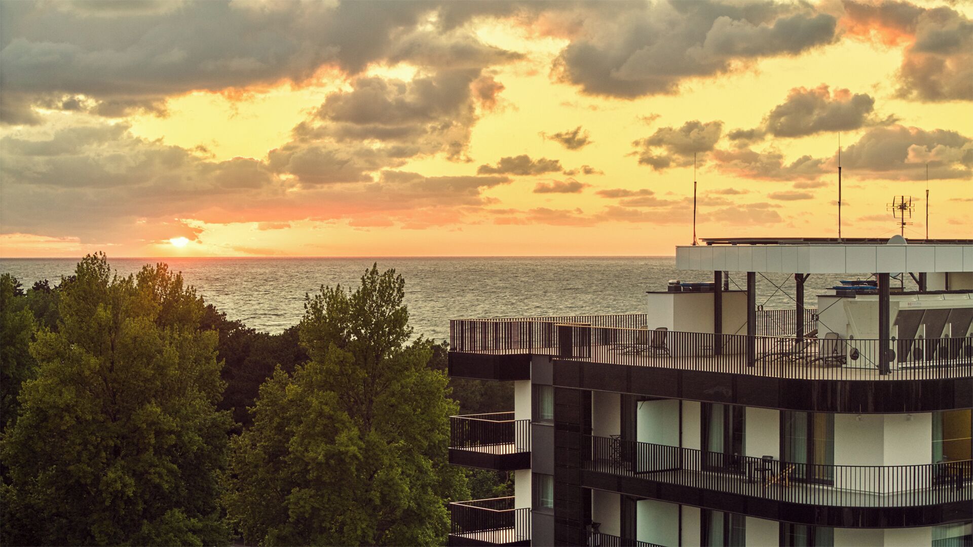 Ein modernes Gebäude mit mehreren Balkonen mit Blick auf ein Gewässer bei Sonnenuntergang.