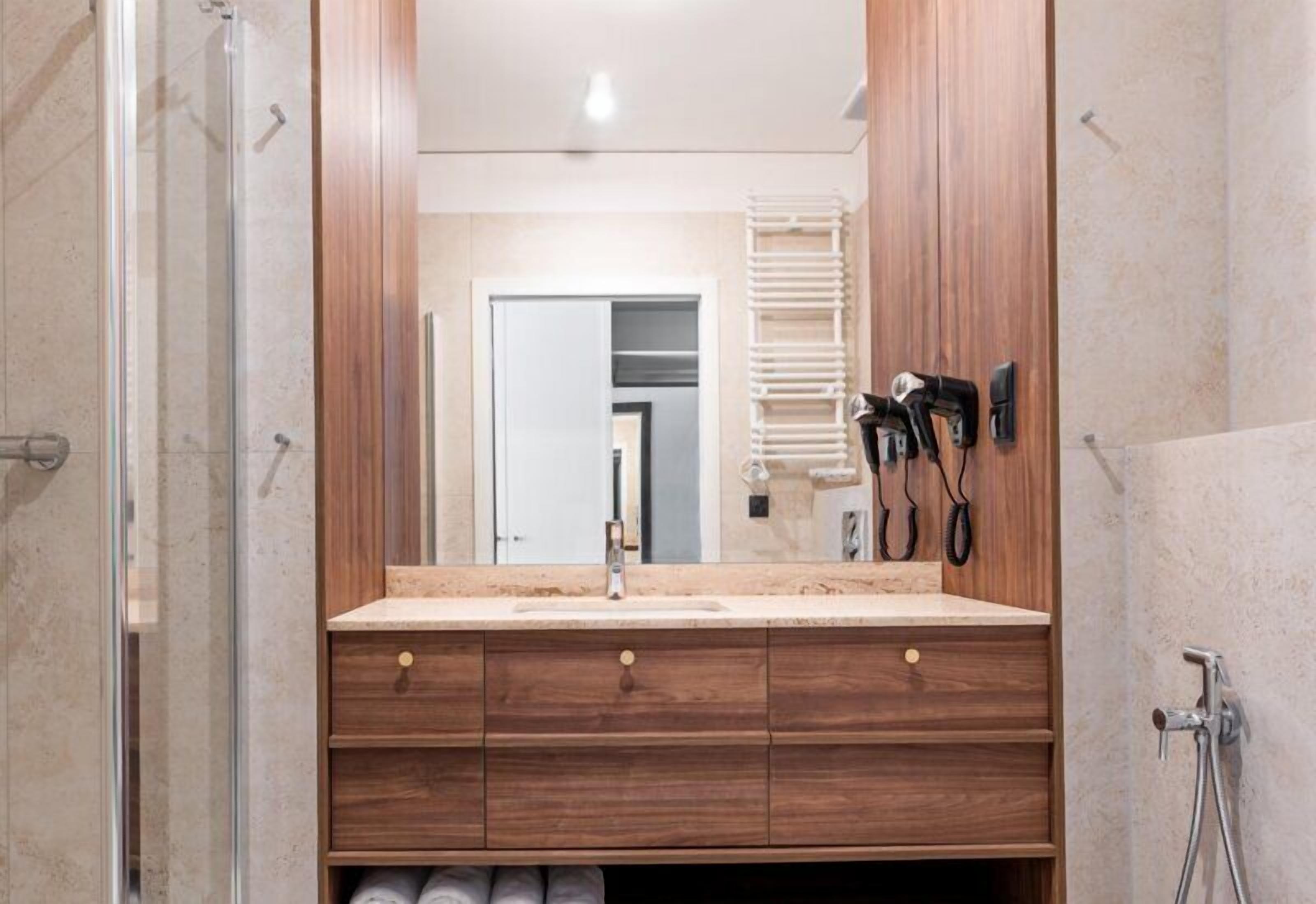 Een badkamer met een houten wastafelmeubel, een spiegel, een douche en een handdoekrek.