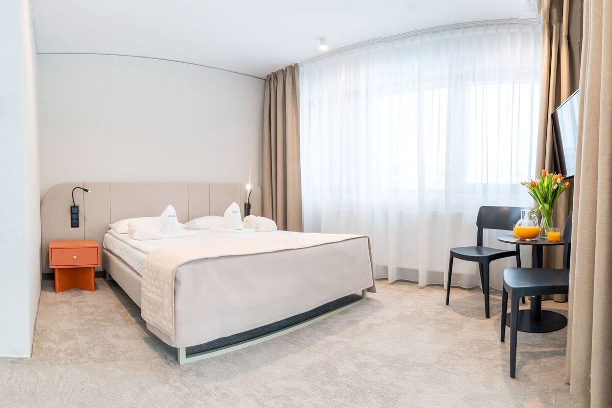 Ein Hotelzimmer mit Bett, Nachttisch, Stuhl, Tisch und einer Vase mit Blumen.