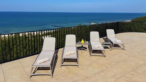 Eine Terrasse mit vier Liegestühlen, einem kleinen Tisch und einer gelben Vase.