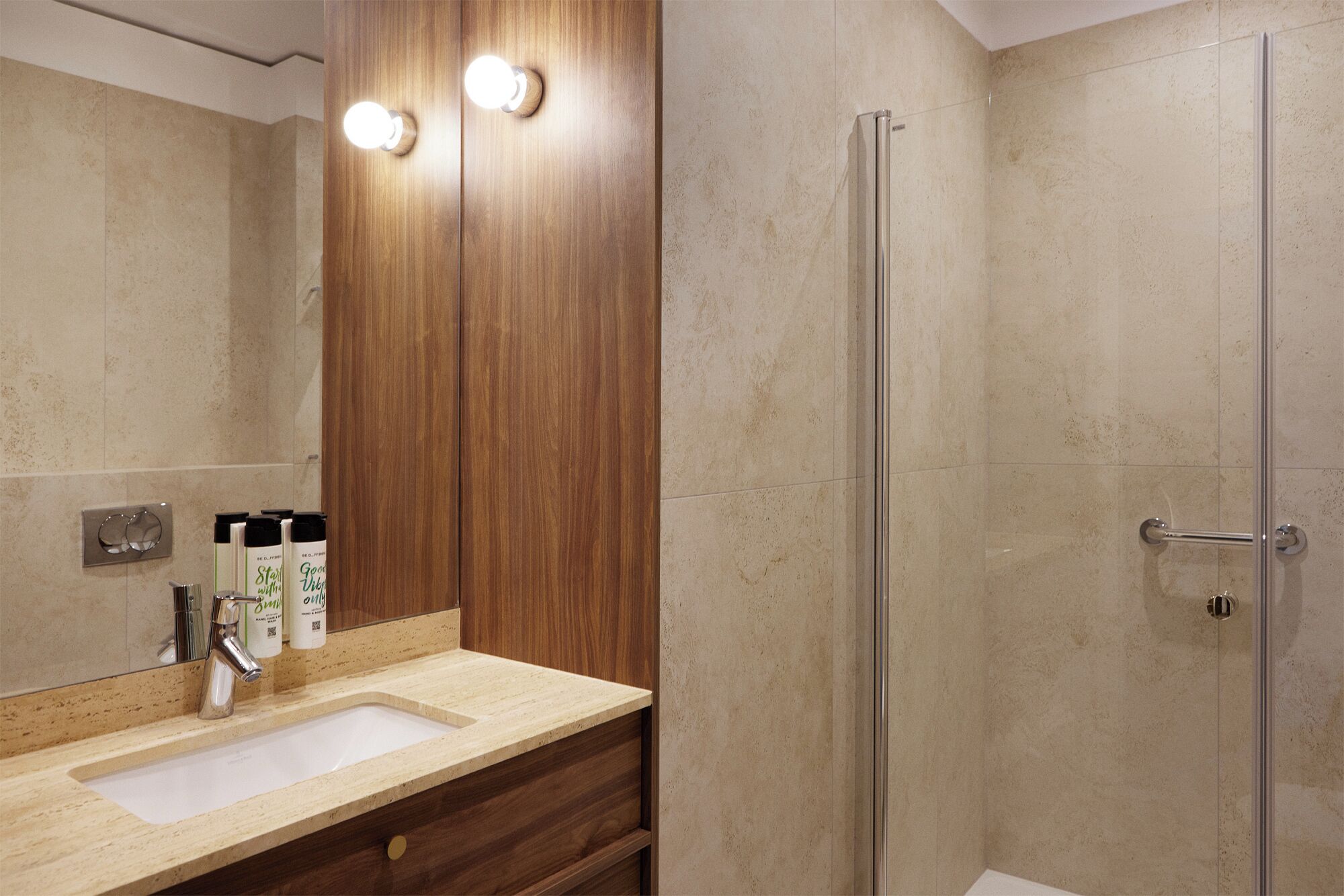 Un baño con tocador de madera, lavamanos y cabina de ducha con mampara de vidrio.