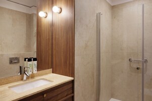 Un baño con tocador de madera, lavamanos y cabina de ducha con mampara de vidrio.