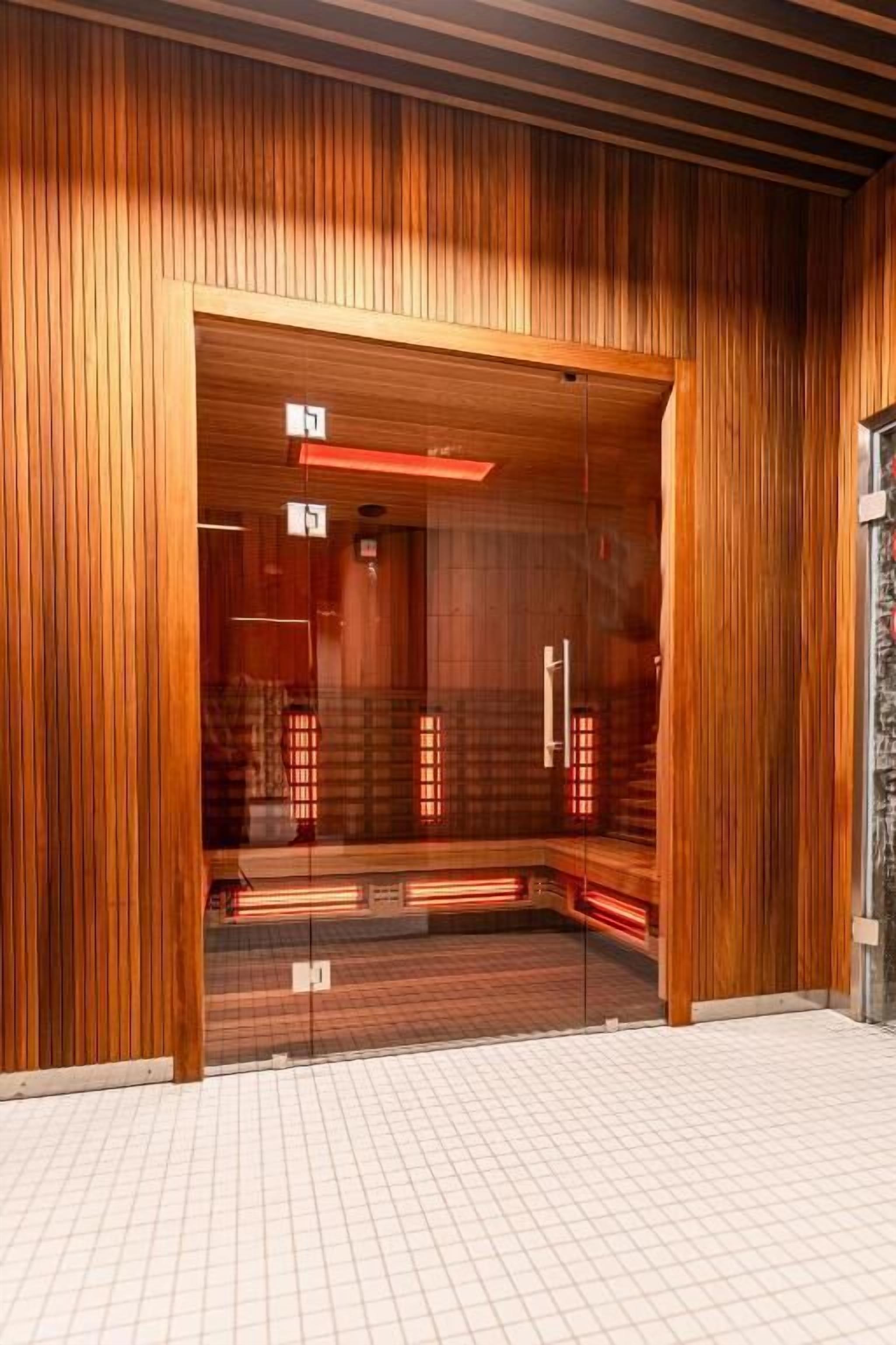 Una sauna con paredes de madera, puertas de vidrio, suelo de baldosas y bancos visibles.