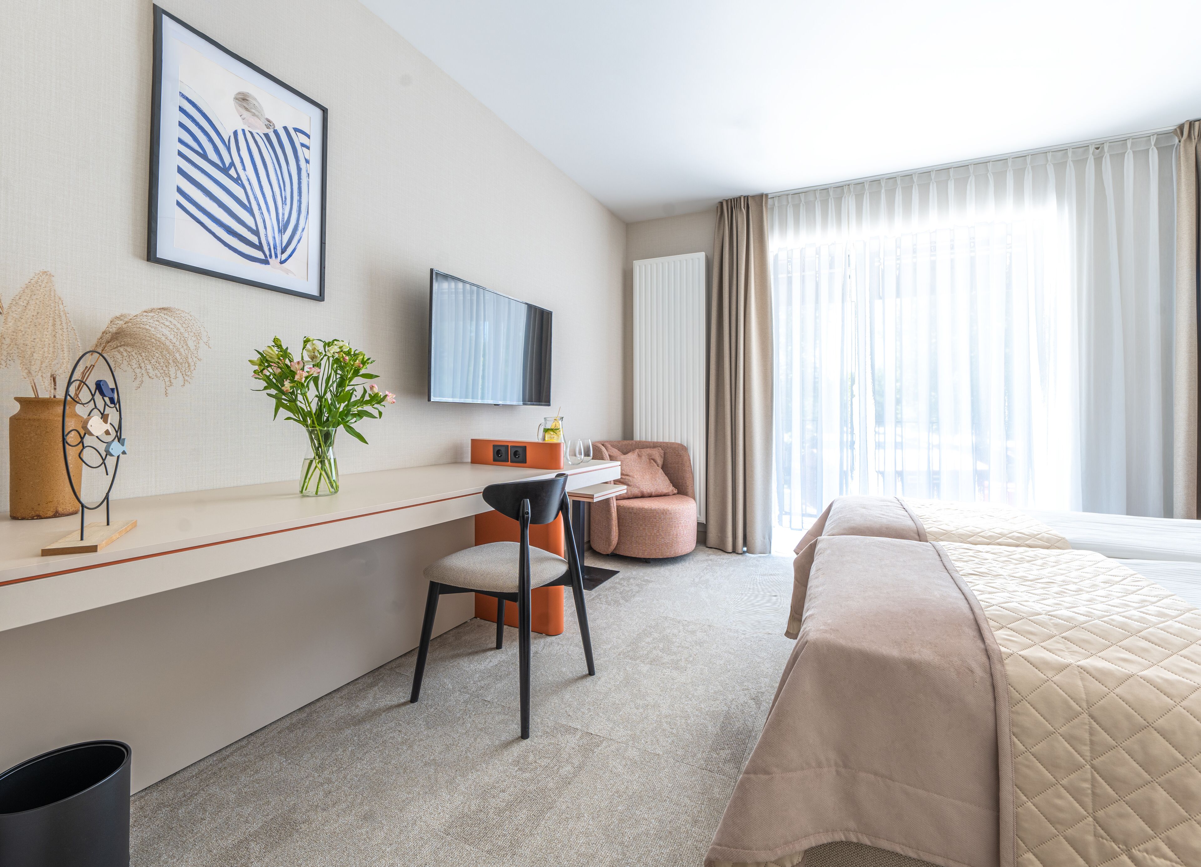 Una habitación de hotel con cama, escritorio, silla, televisión y ventana con cortinas.