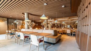 Ein modernes Restaurant mit Holzbalkendecke, mehreren Tischen und Stühlen sowie dekorativen Pflanzen.