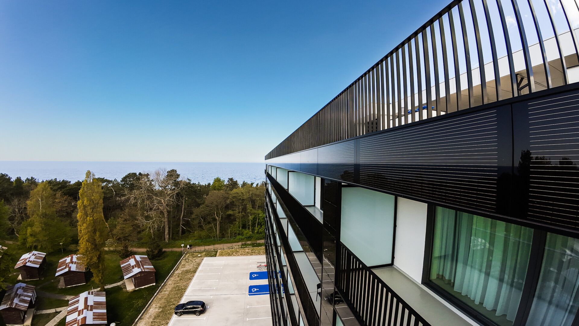 Un edificio moderno con amplios ventanales, un estacionamiento y vista al mar.