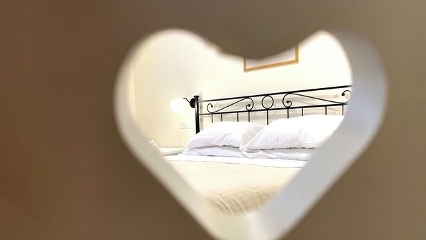 A bed with a metal headboard and white bedding, viewed through a heart-shaped cutout. - Double Room with private bathroom in Terralba (Oristano) - Lentisco (Terralba)