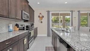 Una cocina moderna con armarios de madera oscura, encimera de granito, microondas integrado y un amplio ventanal con vistas a la vegetación.