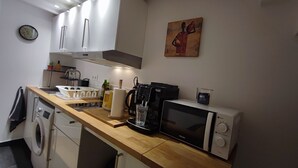 A compact kitchen with a microwave, toaster, and coffee machine. There is a sink, a dish rack, and a clock on the wall. - Jardin Secret Greenhouse (Ivry-sur-Seine)