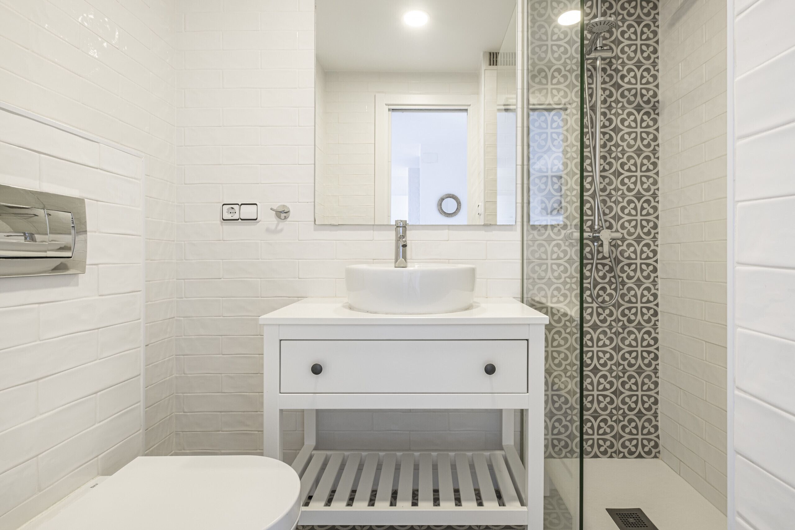 A modern bathroom with white tiles, a white sink, and a shower with patterned tiles.