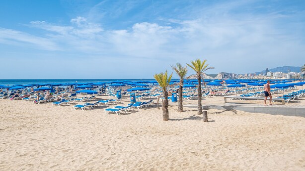 A beach with numerous blue umbrellas and sun loungers.