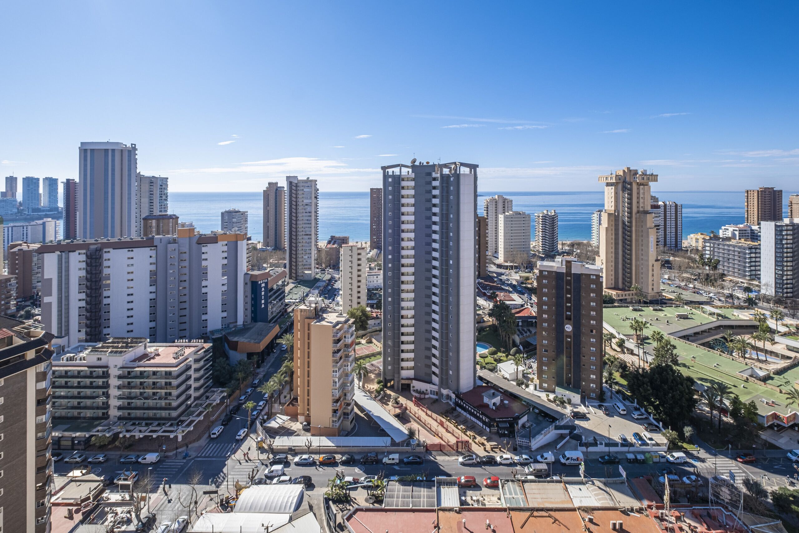 A high-rise building with a modern design, surrounded by other tall buildings and a clear blue sky.
