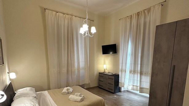 A modern bedroom with a bed, bedside table, dresser, and a TV mounted on the wall. - Double Room with private bathroom in Terralba (Oristano) - Juniper (Terralba)