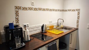 A compact kitchen with a coffee machine, kettle, and a yellow dish rack.
