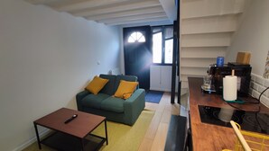 A compact living space with a green sofa, a small table, and a kitchenette area.