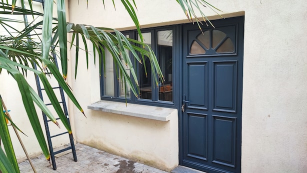 A dark blue door with a window above it, a small ledge, and a ladder leaning against a wall.