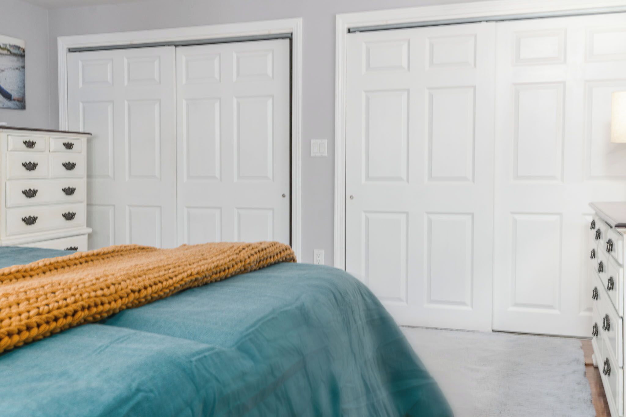A bedroom with a bed, a dresser, and two white doors.