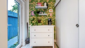 Een smalle gang met een witte dressoir, planken met decoratieve objecten en behang met een patroon.