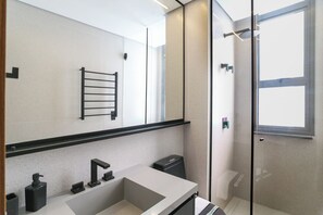 Ein modernes Badezimmer mit großem Spiegel, Handtuchhalter, Waschbecken und Duschbereich.