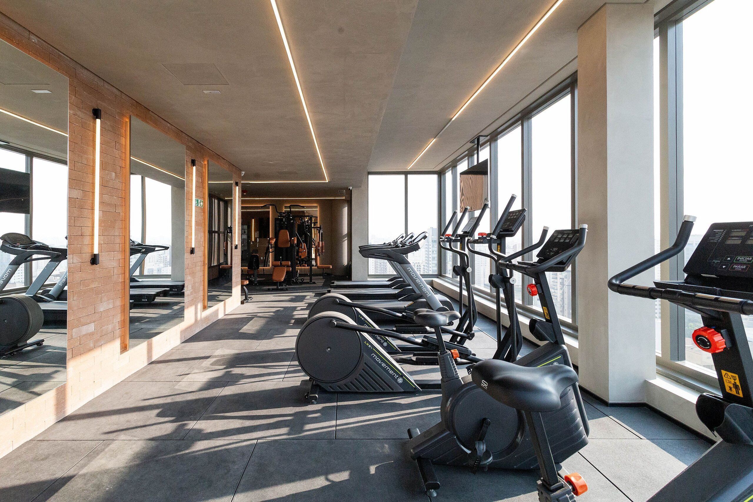Une salle de sport équipée de matériel d’exercice, dotée de grandes fenêtres et d’un sol en béton.