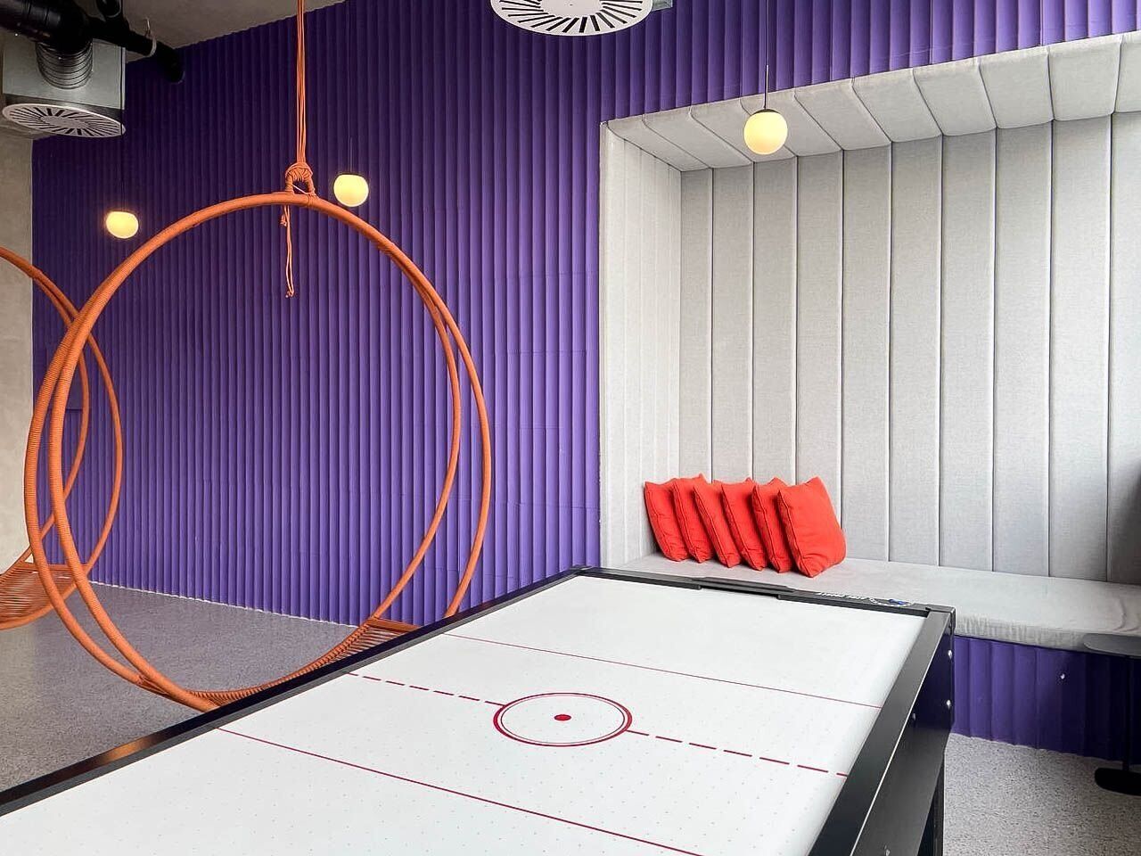 A room with a foosball table, orange rings, and a window with red cushions.