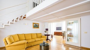 Una sala de estar con un sofá amarillo, una mesa redonda de centro, una escalera y una estantería.