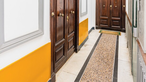 Un pasillo con puertas dobles, una pared amarillo y blanca, y un piso moteado.