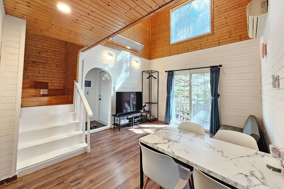 Una habitación amplia con techo de madera, una mesa de mármol y una escalera que conduce a otra zona.