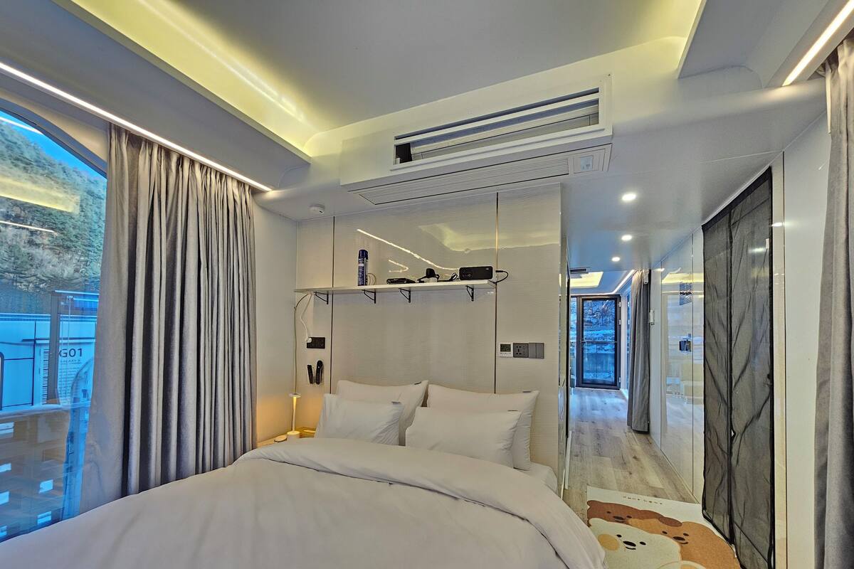 Una habitación de hotel moderna con una cama grande, un armario empotrado, aire acondicionado instalado en el techo y vistas a un paisaje nevado a través de un ventanal amplio.