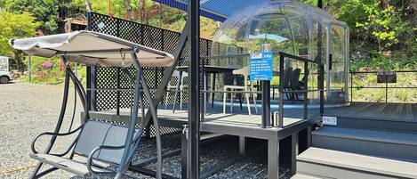 A covered outdoor seating area with a table and chairs, a transparent dome structure, and a blue canopy.