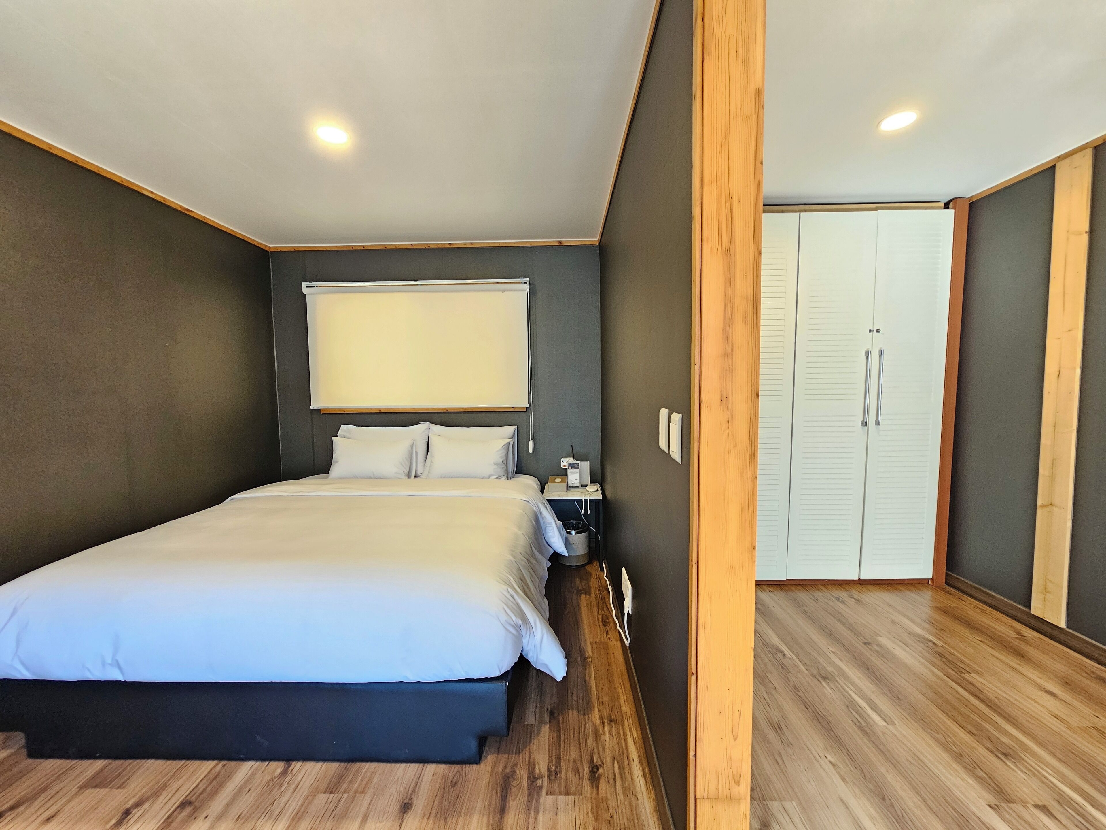 Un dormitorio moderno con una cama grande, una mesita de noche, un armario y una ventana con persianas.