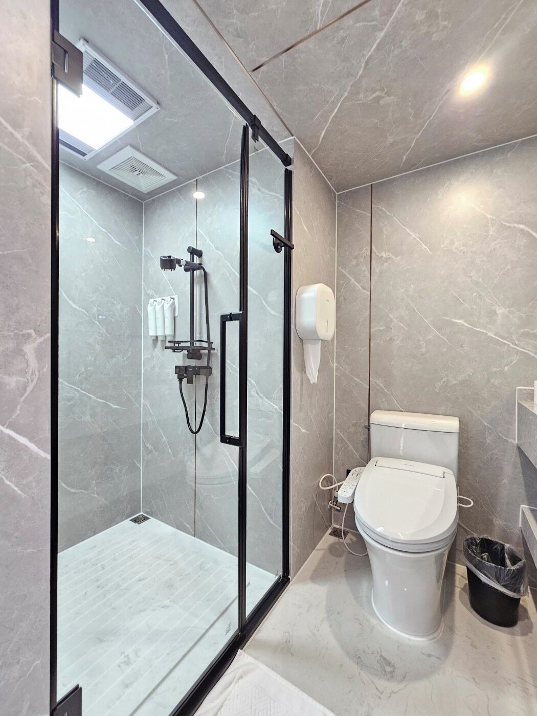 Un baño moderno con ducha envuelta en vidrio, inodoro y secamanos.