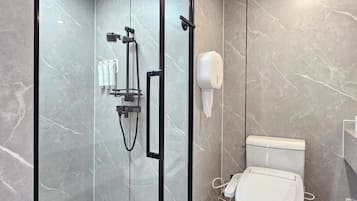 Un baño moderno con ducha envuelta en vidrio, inodoro y secamanos.