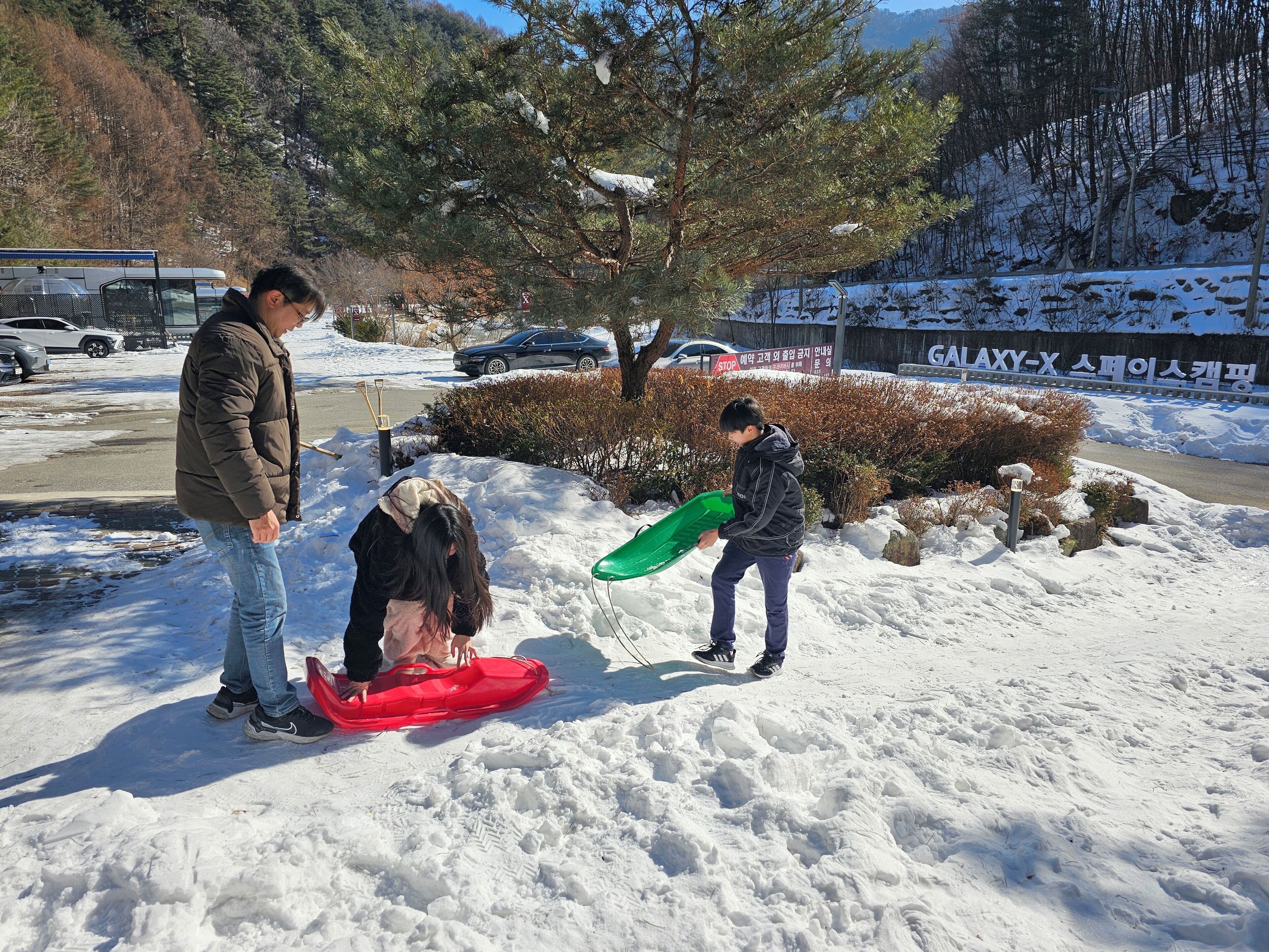 A snowy outdoor area with a red sled and a green snowboard.
