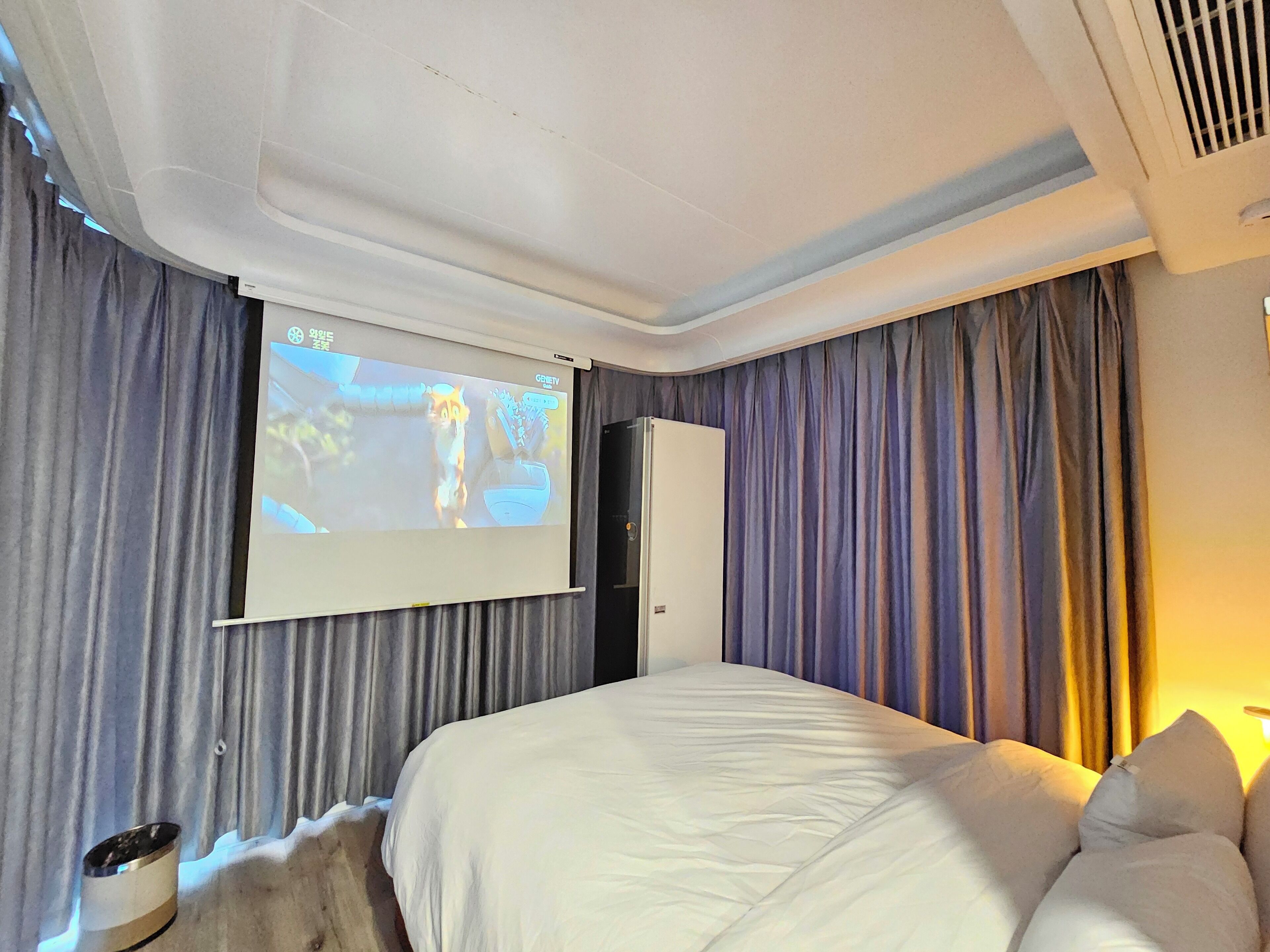 A hotel room with a large bed, a projector screen, and curtains.