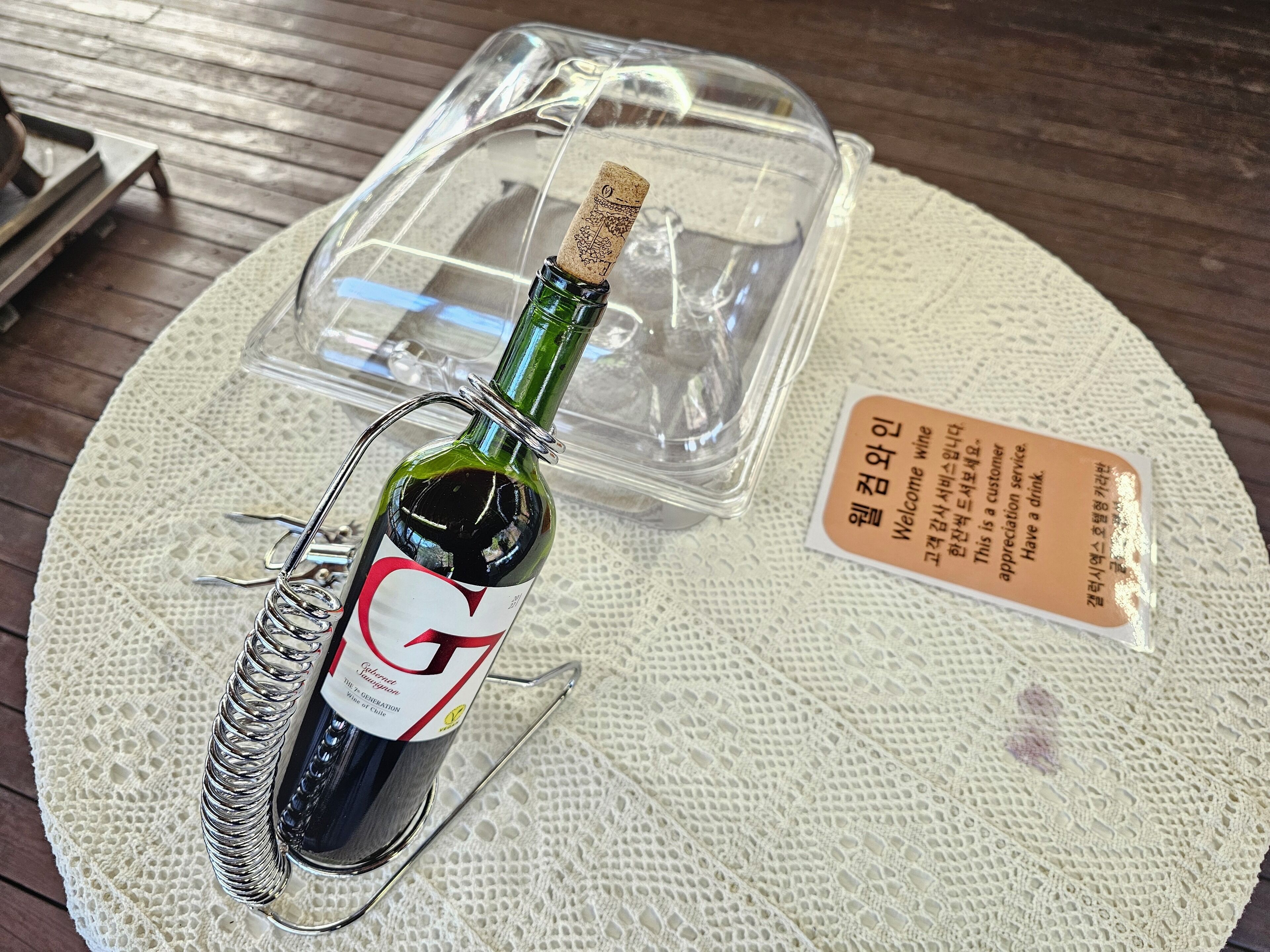 Una botella de vino con un corcho, una copa y una etiqueta sobre una mesa con posavasos.