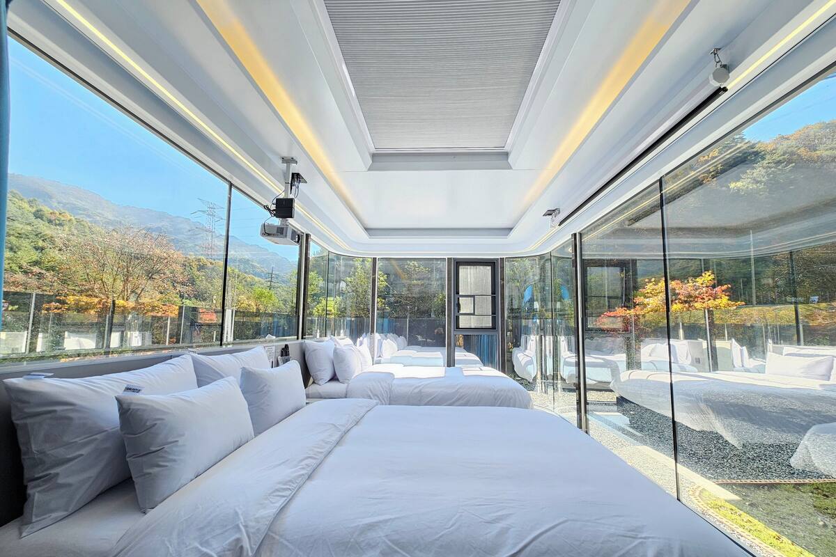 Un dormitorio moderno con una cama grande, paredes de vidrio y vistas a un paisaje montañoso.