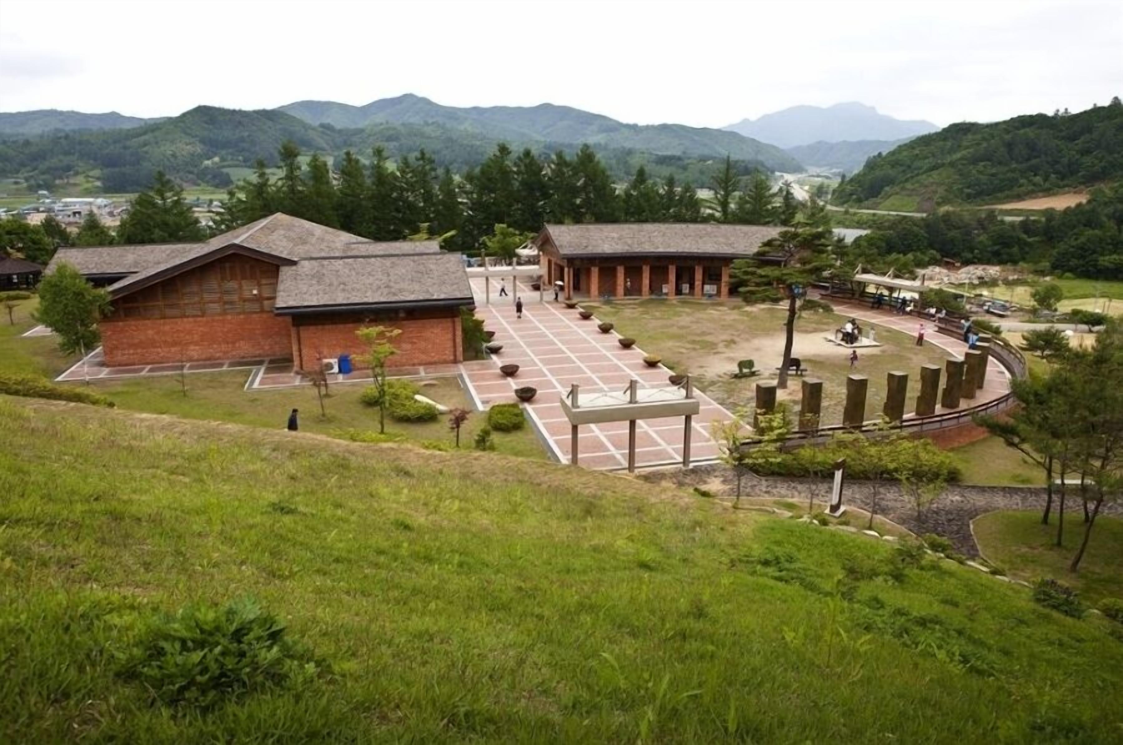 A building with a brick facade and a sloped roof, surrounded by a landscaped area with pathways and benches.