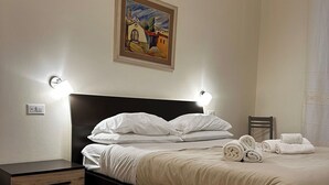 A neatly made bed with white linens and rolled towels, a dark headboard, and a painting above it. - Double Room with private bathroom in Terralba (Oristano) – Ginestra (Terralba)