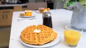 A waffle with butter and a glass of orange juice on a white table. - The Kulshan Hotel (Sedro-Woolley)