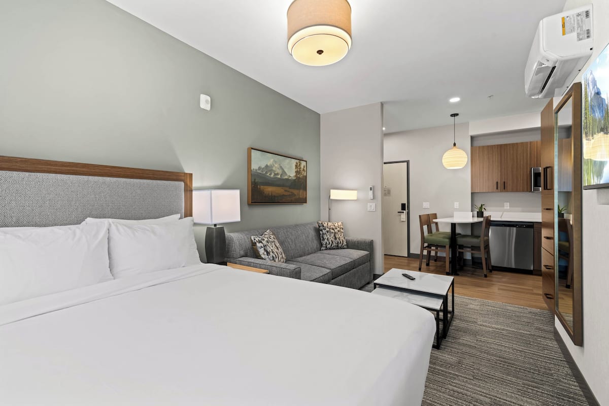 Ein modernes Hotelzimmer mit einem großen Bett, einem grauen Sofa, einem Essbereich und einer Küche.