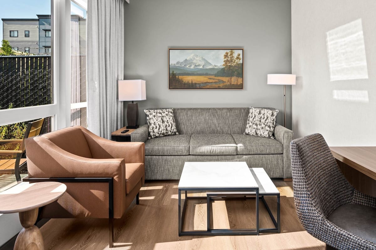 Ein modernes Wohnzimmer mit einem grauen Sofa, gemusterten Kissen, einem Holztisch und einem Ledersessel mit Fischgrätmuster.