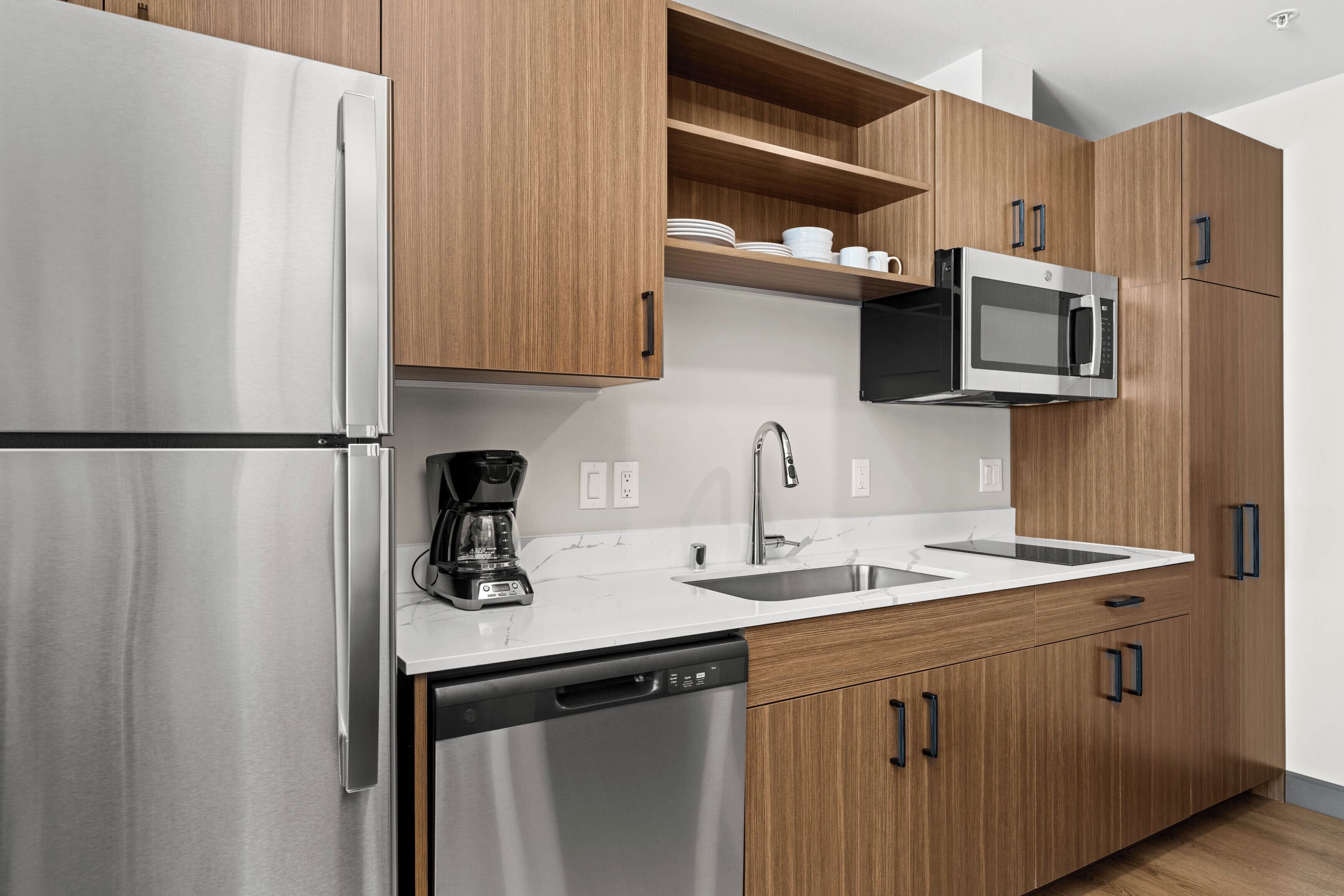 Una cocina moderna con electrodomésticos de acero inoxidable, armarios de madera y una encimera blanca.