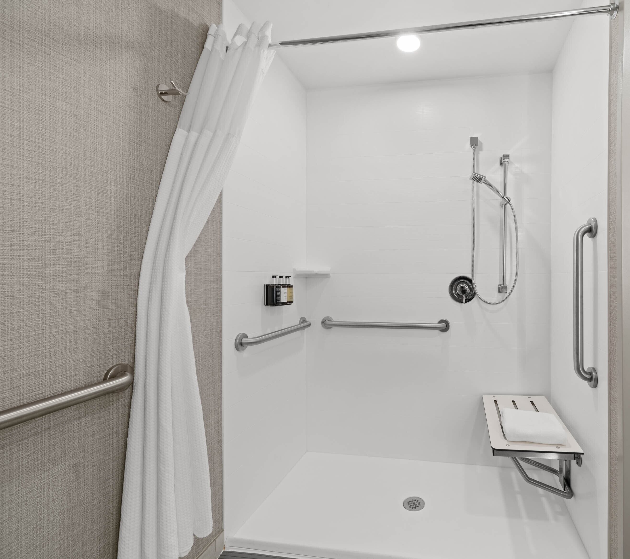 A modern shower area with a glass door, a handheld showerhead, a handheld showerhead, a towel rack, and a soap dispenser.