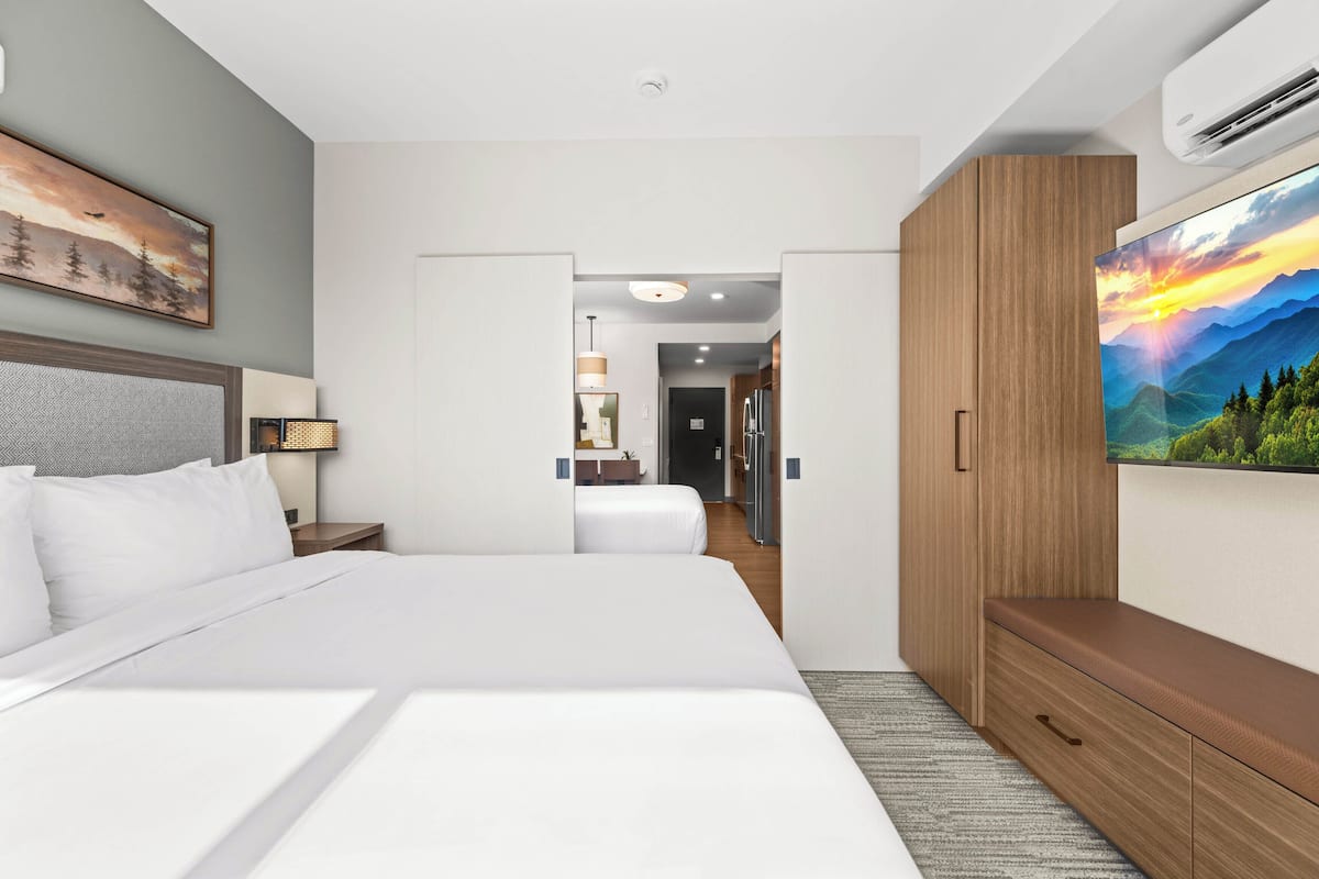 Ein modernes Hotelzimmer mit einem großen Bett, einem Holzschrank, einem Flachbildfernseher und einem Gemälde an der Wand.