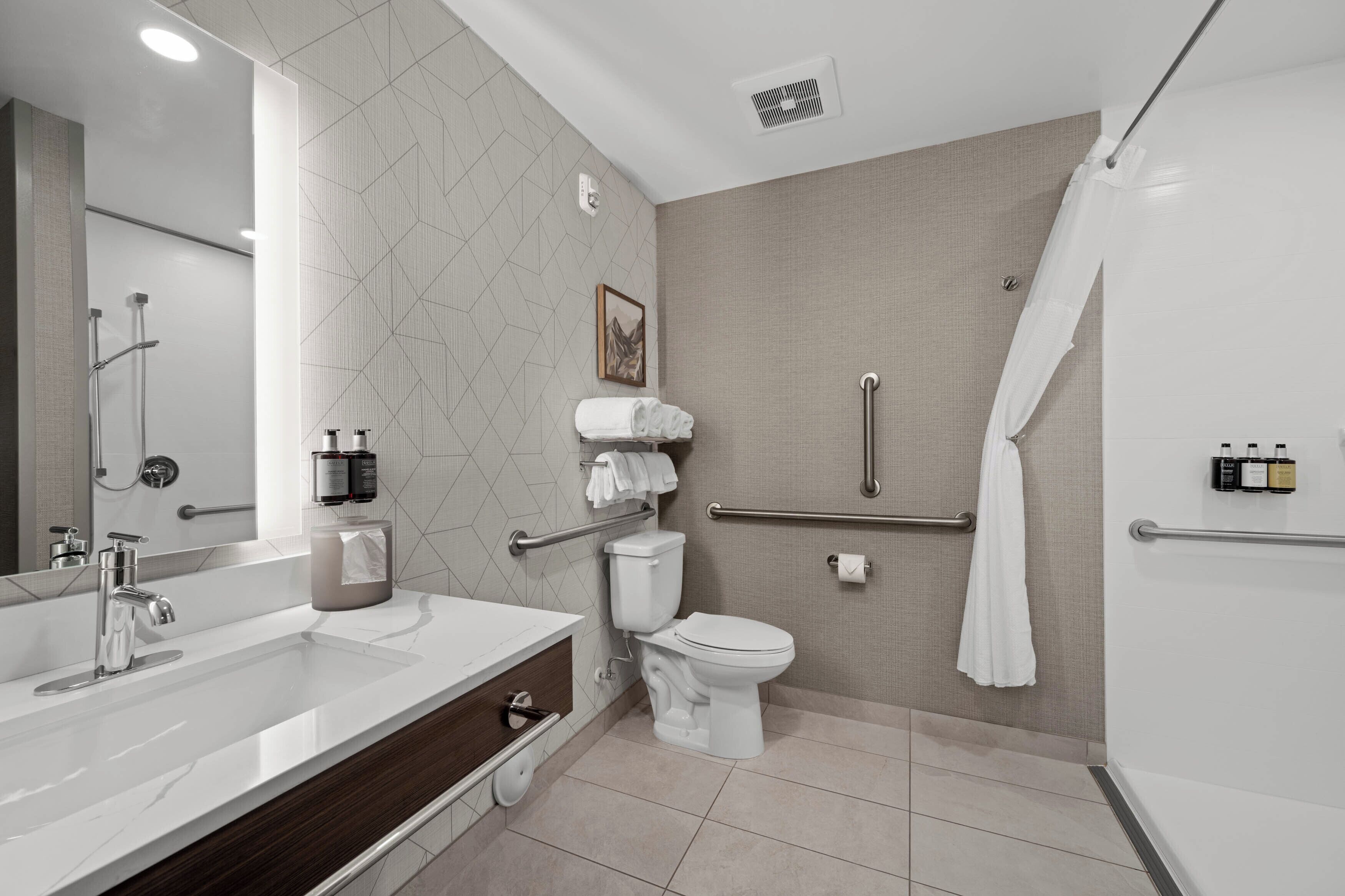 A modern bathroom with a large mirror, a dual sink vanity, a toilet, and a shower area.