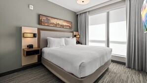 A hotel room with a large bed, a headboard with a painting, bedside lamps, a nightstand, and a large window with curtains. - The Kulshan Hotel (Sedro-Woolley)